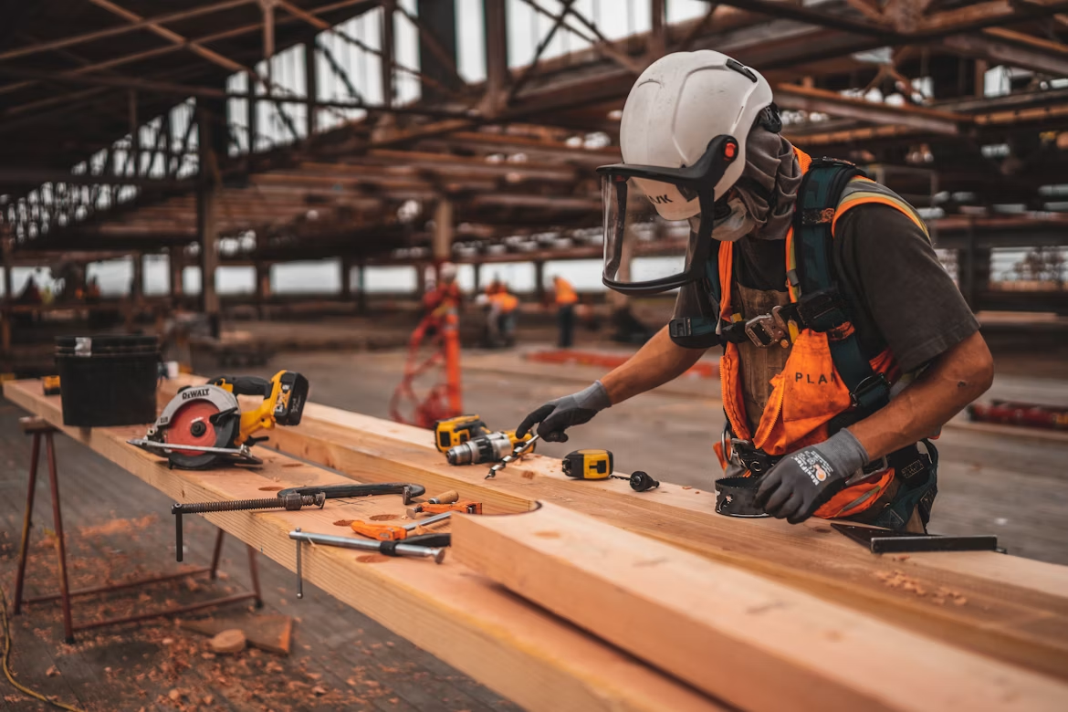 man in orange and black vest wearing white helmet holding yellow and black power tool (1)